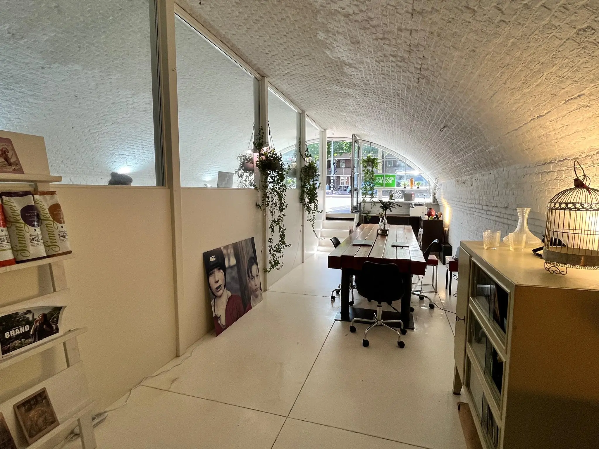 Een sfeervolle werkruimte met gebogen plafond van baksteen, een grote houten tafel, planten en kunst aan de muur bij Tussen de Bogen.
